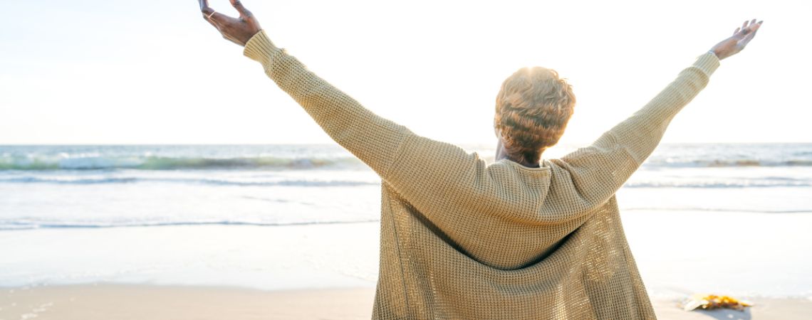woman on beach with hands up to sky